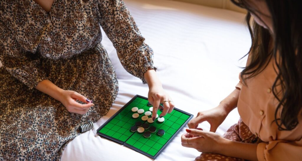 crop-unrecognizable-women-playing-reversi-game-on-bed
