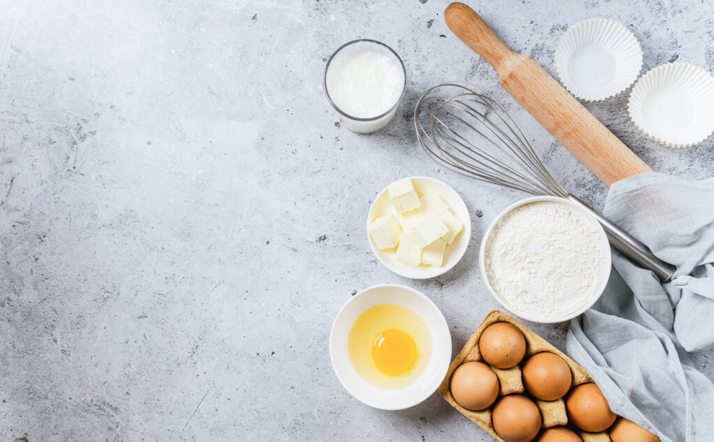 Bakery background. Bake ingredient for recipe Easter cake or dessert, pie. Egg and flour, butter and kitchen textile grey stone table. Top view, copy space.