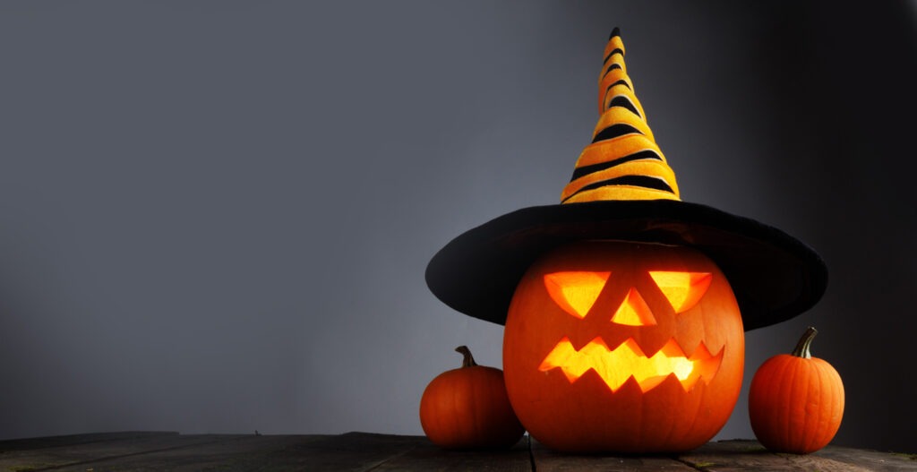 Jack O Lantern Halloween funny pumpkin with a carved smiling face with a witches hat on gray background with copy space for text