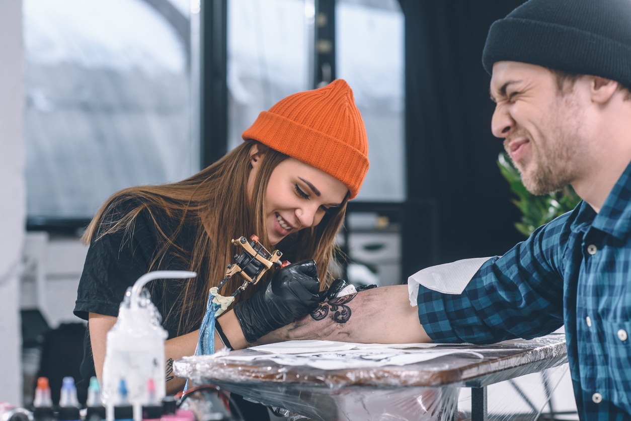 Man with grimace of pain during tattooing process in studio
