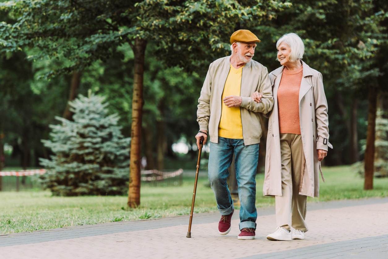 a senior man using a cane while walking with his wife