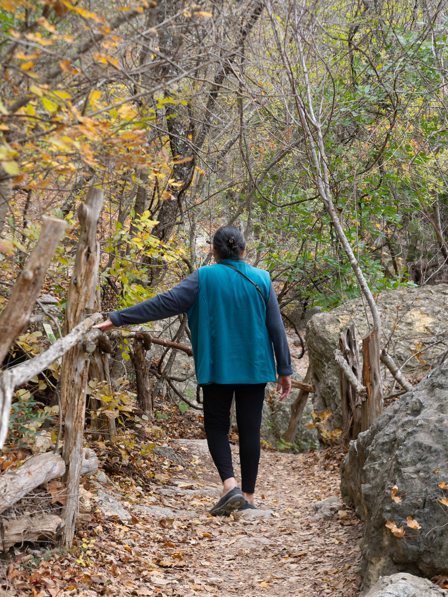 Senior woman wearing a turquoise vest walking on a wooded trail during autumn