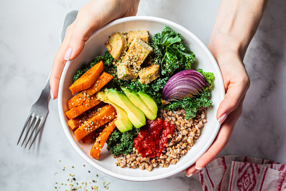 Baked vegetables, avocado, tofu and buckwheat buddha bowl. Vegan lunch salad with kale, baked sweet potato, tofu, buckwheat and avocado in a white bowl. Vegan concept