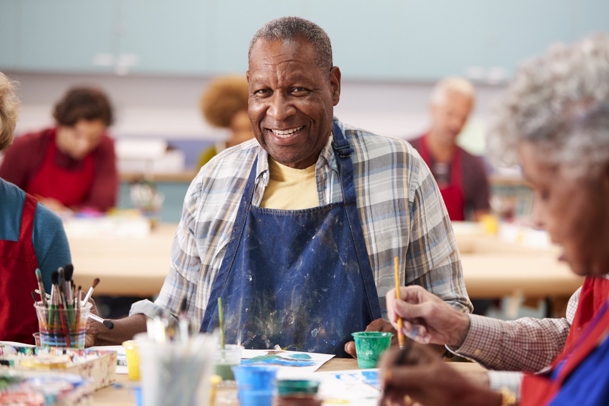 a happy elderly man painting with an apron on