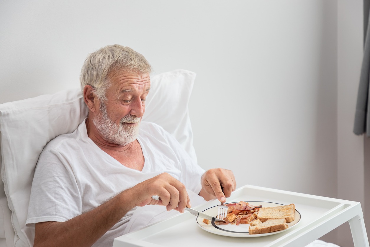 elderly man eating breakfast in bed using an overbed table