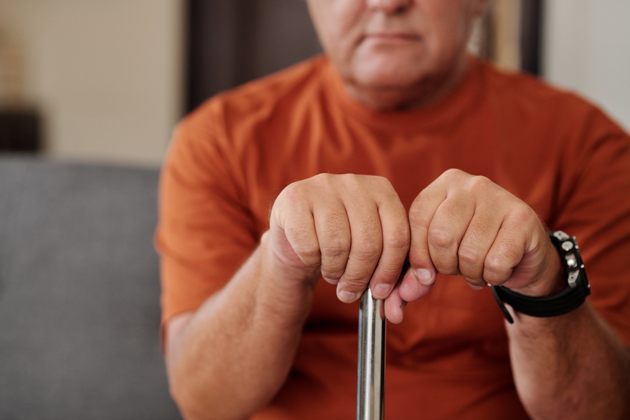 elderly man holding onto a cane while sitting on a sofa