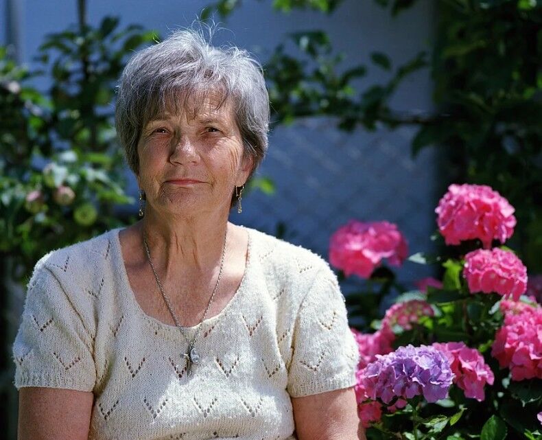 Elderly woman sitting in front of flowers