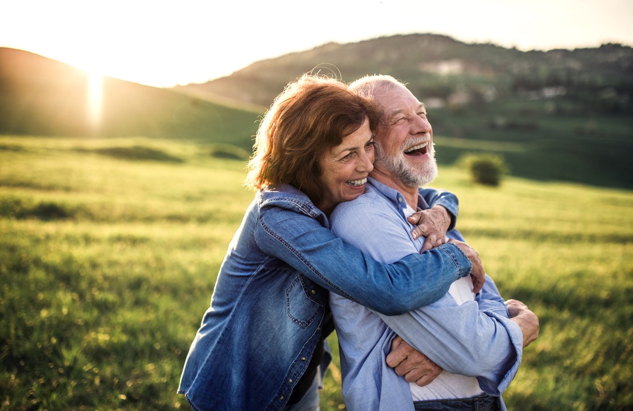 Happy senior couple outside in spring nature, hugging at sunset. Side view