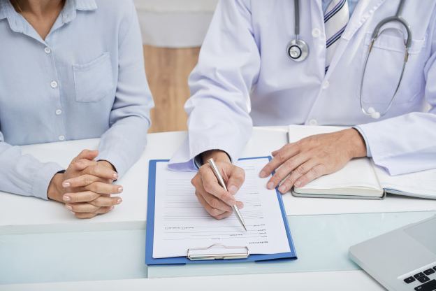 Image of a Doctor filling in a patient's medical history on a table.
