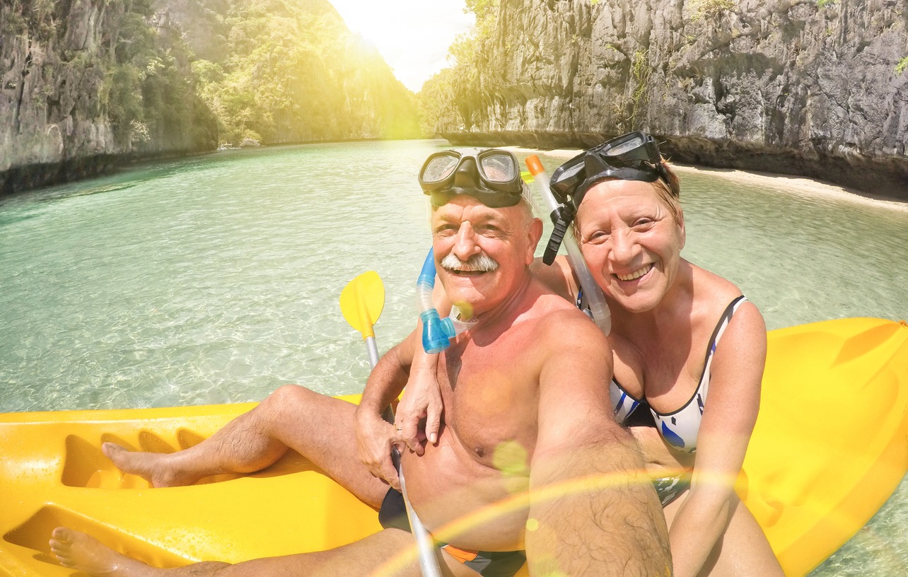 Senior happy couple taking selfie on a kayak at Big Lagoon in El Nido Palawan - Travel to Philippines wonders - Active elderly concept around the world - Lens flare and sun halo are part of the composition