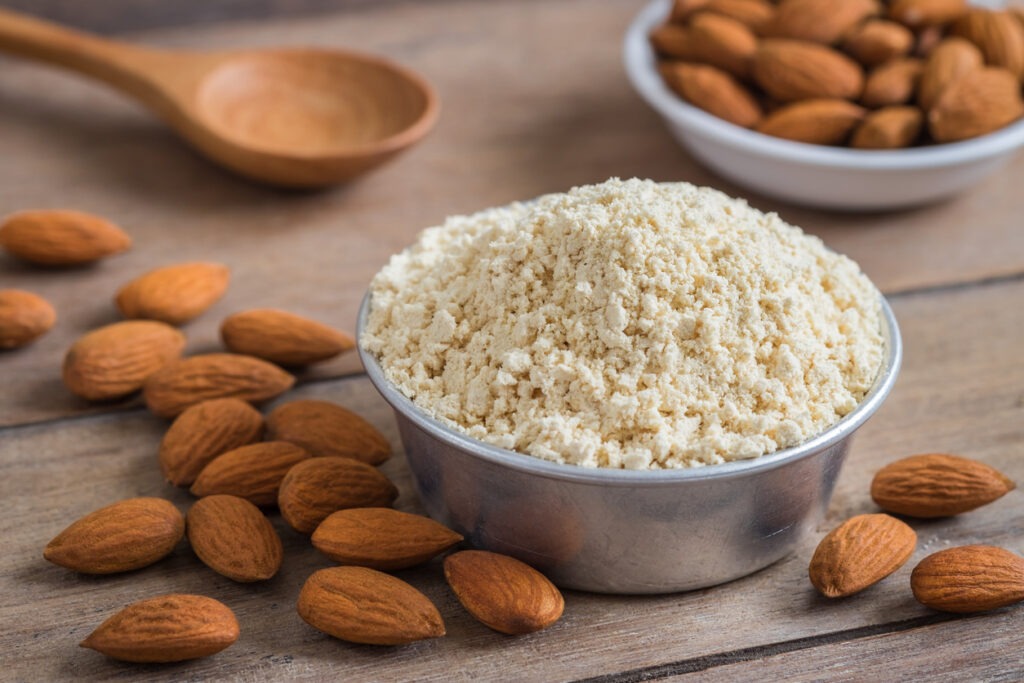 Almond flour in bowl and almonds on a wooden table