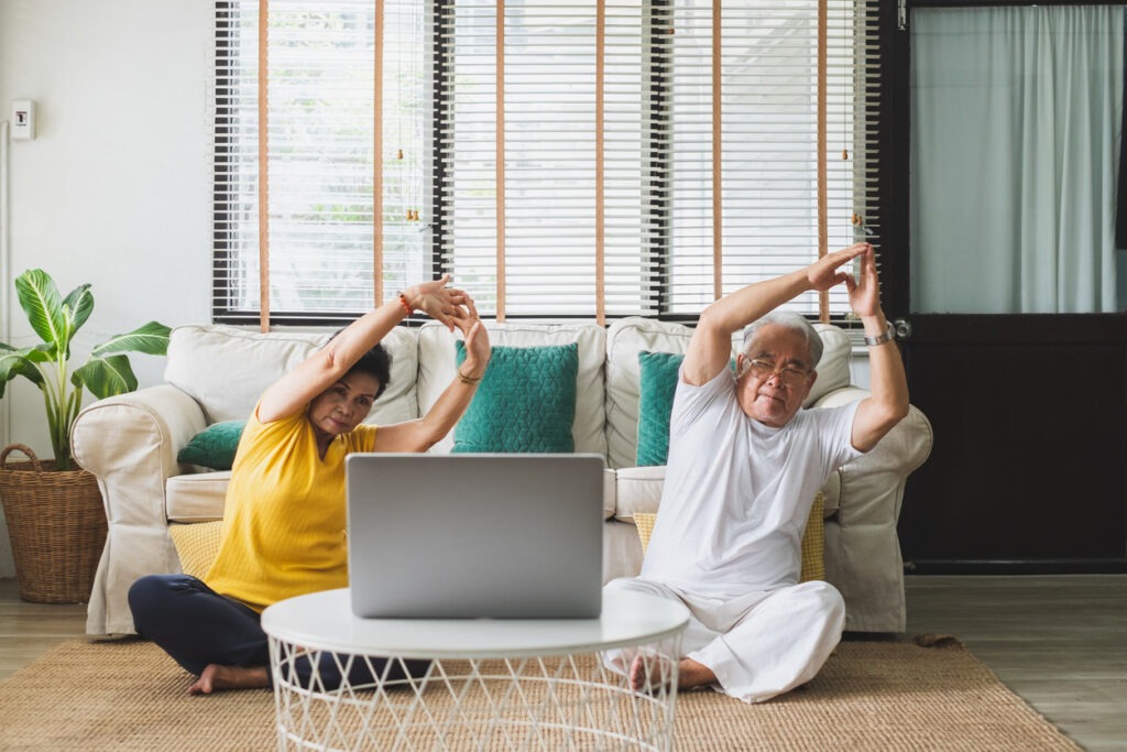 A couple of seniors doing yoga at home while following an instructional video on a laptop