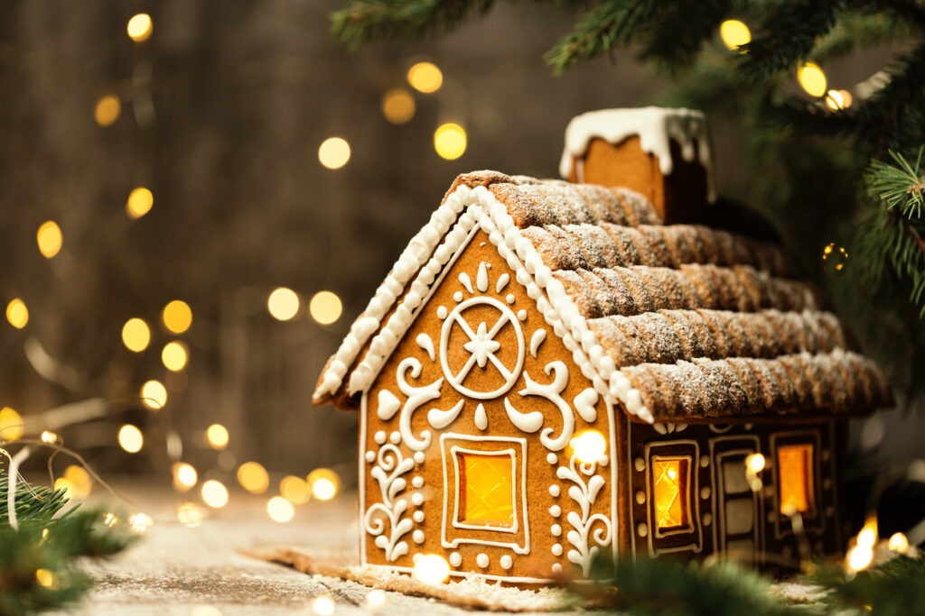 Christmas Gingerbread House with Window Xmas Lights over shining Garland. Winter Holiday Ginger Bread Cake with White Sweet Icing over Dark Fantasy unfocused Background. Merry Christmas Card Design