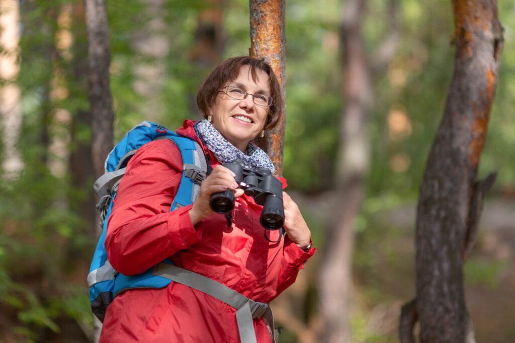 Senior woman with binoculars in a forest. Active lifestyle concept at the age after 60
