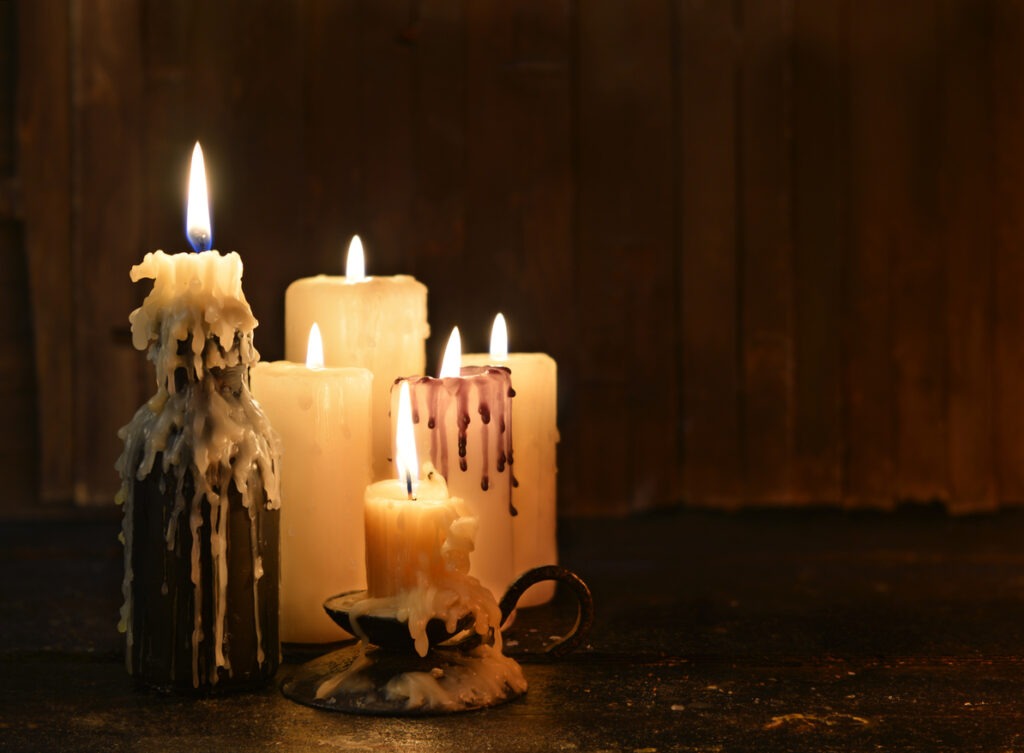 Group of evil candles burning in the darkness and copy space on wooden background. Black magic ritual or scary Halloween rite