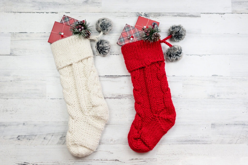 Knitted Christmas stockings on white wooden background - holiday gift giving
