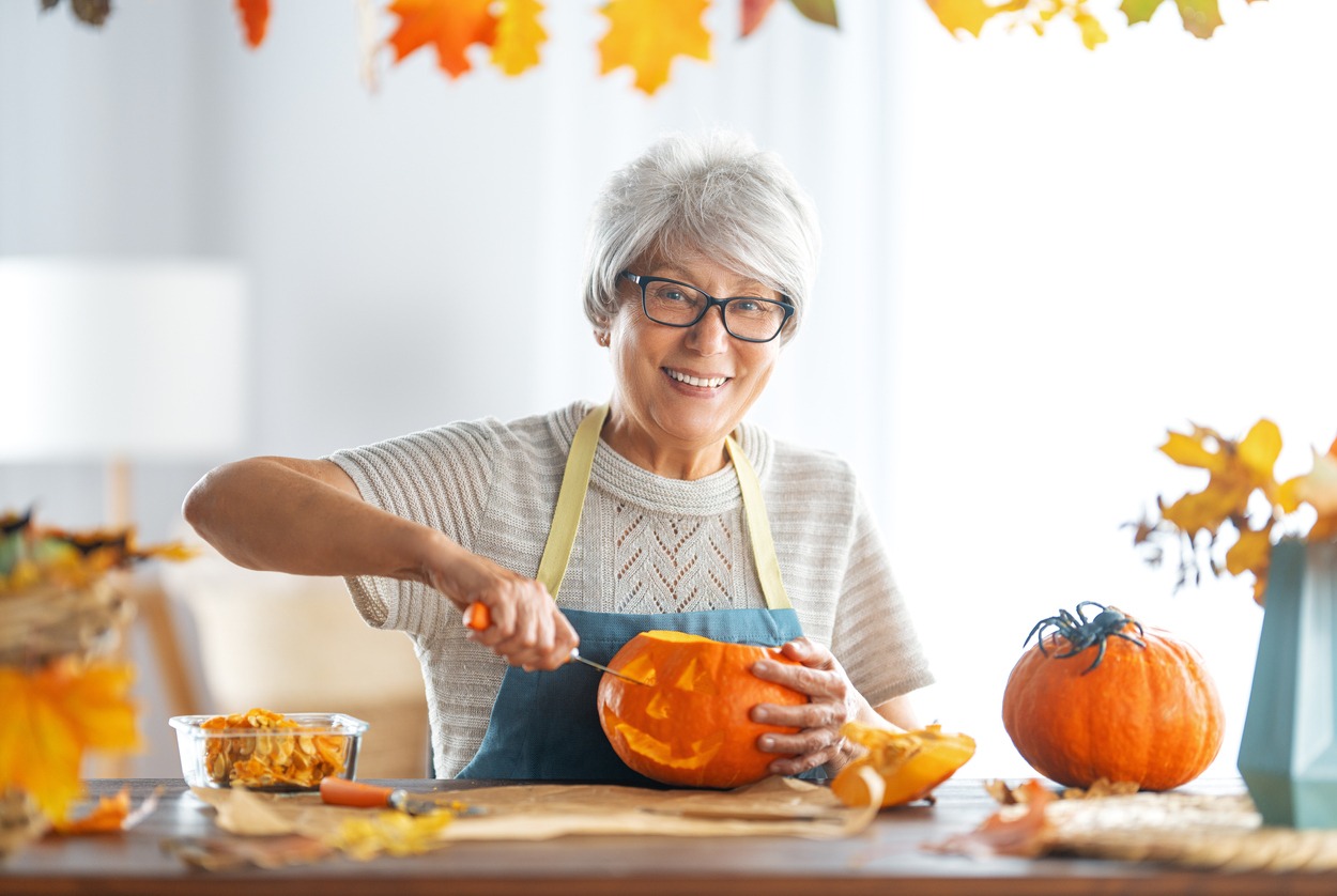 Happy Halloween! The senior woman is carving a pumpkin. Family preparing for a holiday