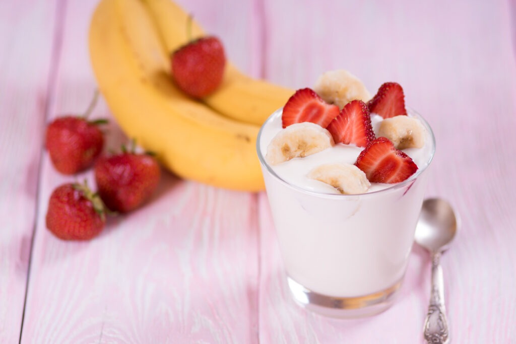 Yogurt with strawberries and banana in a glass. Pink background