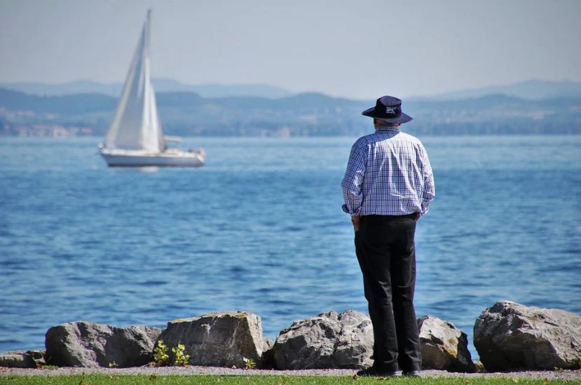 An elderly person looking at a sailboat.