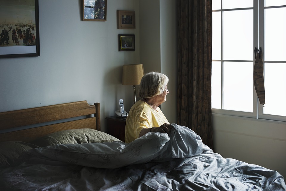 an-older-person-in-bed-looking-out-the-window