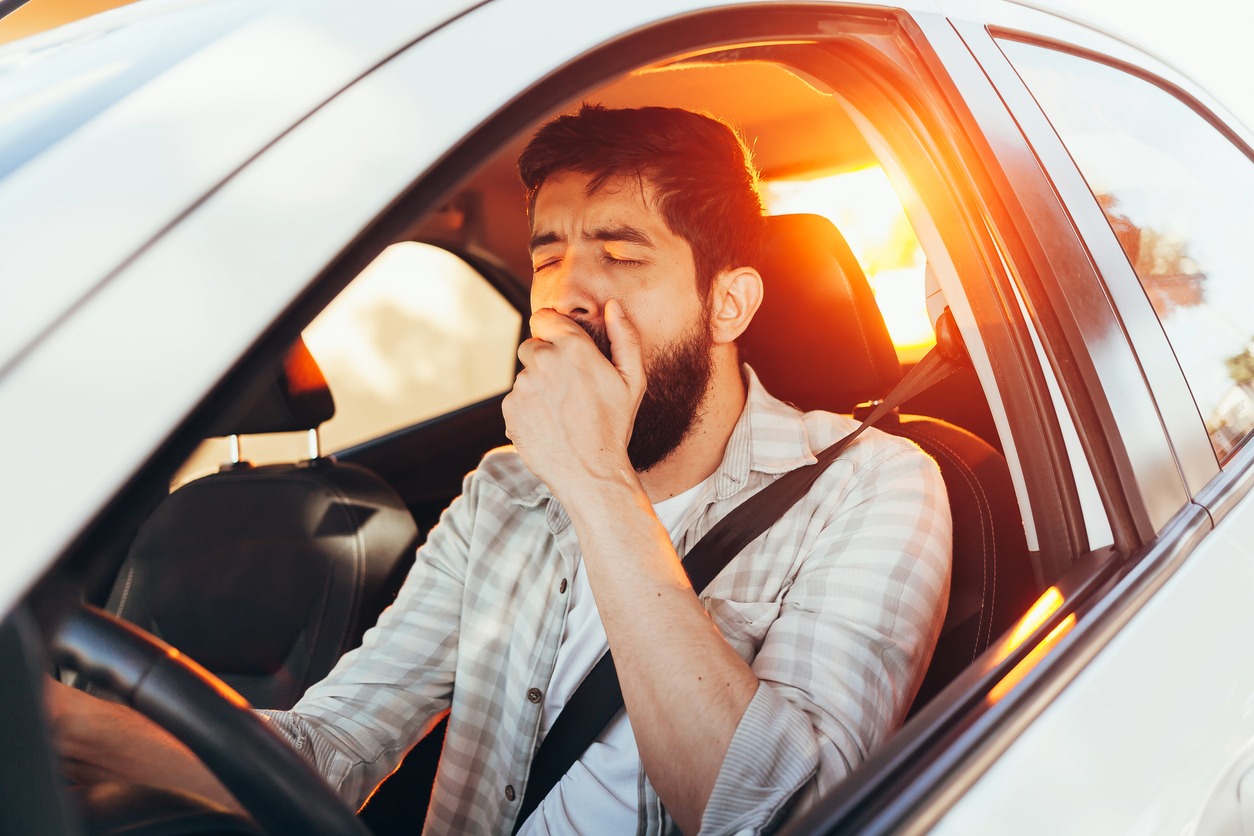 A man yawning while driving his car