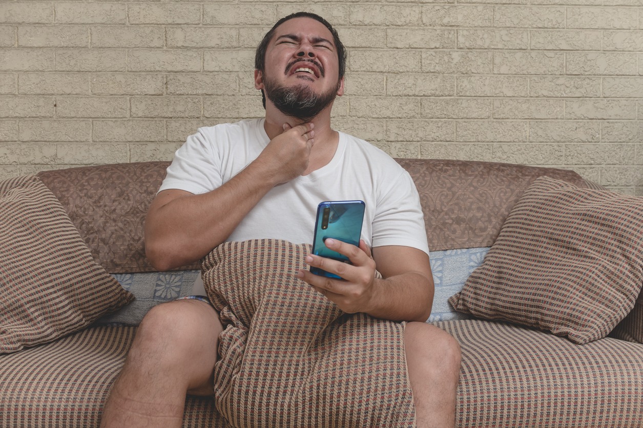 A man experiencing painful or itchy throat while sitting on a couch