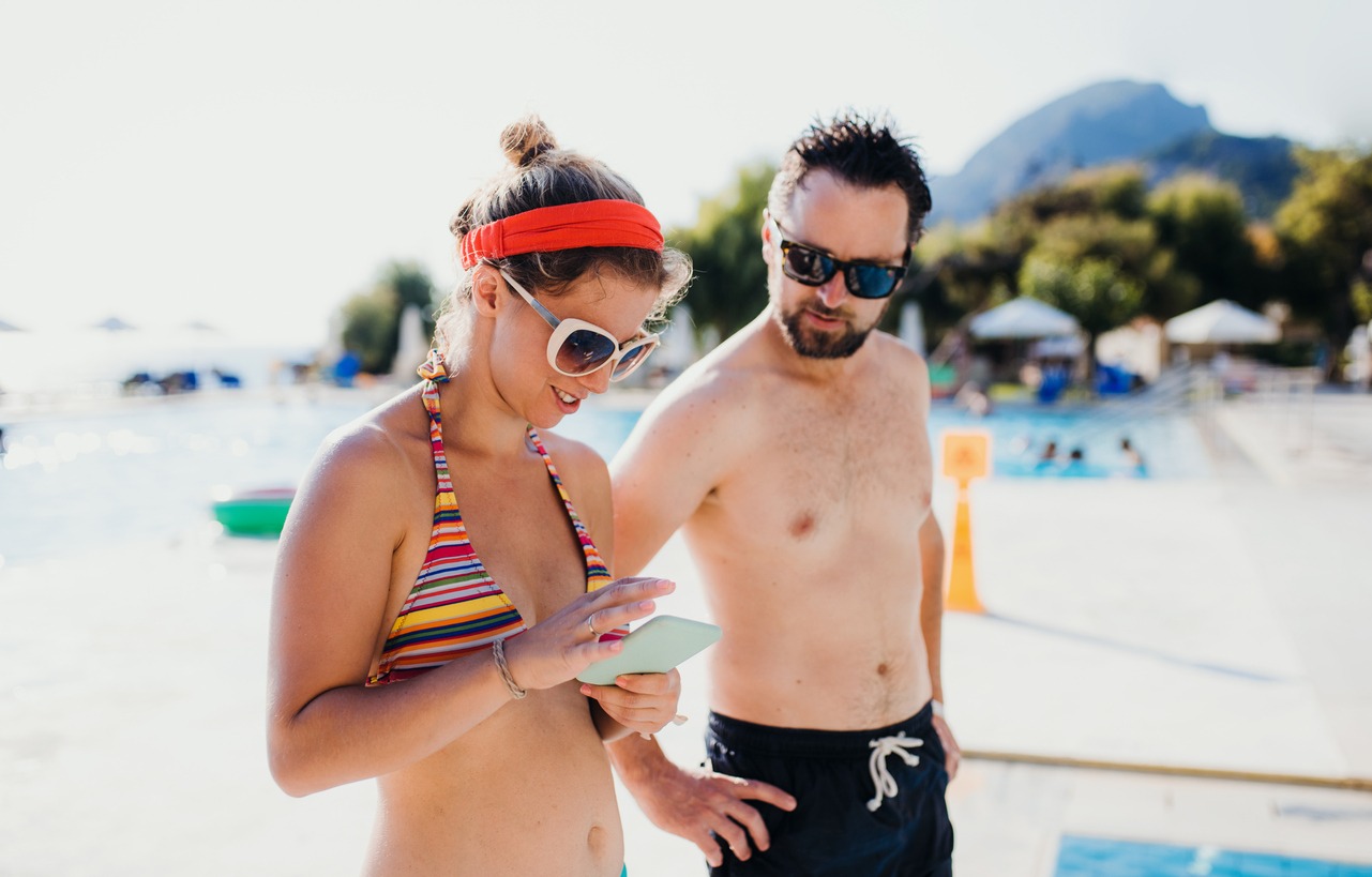 a-couple-in-swimsuit-by-the-swimming-pool-on-summer-holiday-using-a-smartphone