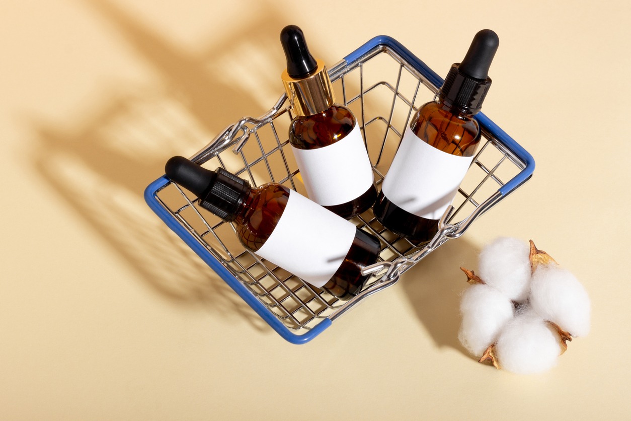 A set of cosmetic products with a dropper for facial skin care in a shopping trolley on a yellow background with shadows. The concept of buying cosmetics, online shopping