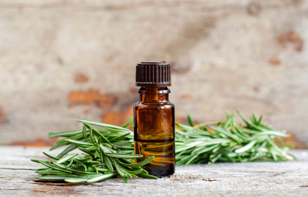 Small bottle of essential rosemary oil on the old wooden background. Aromatherapy, spa and herbal medicine ingredients. Copy space.