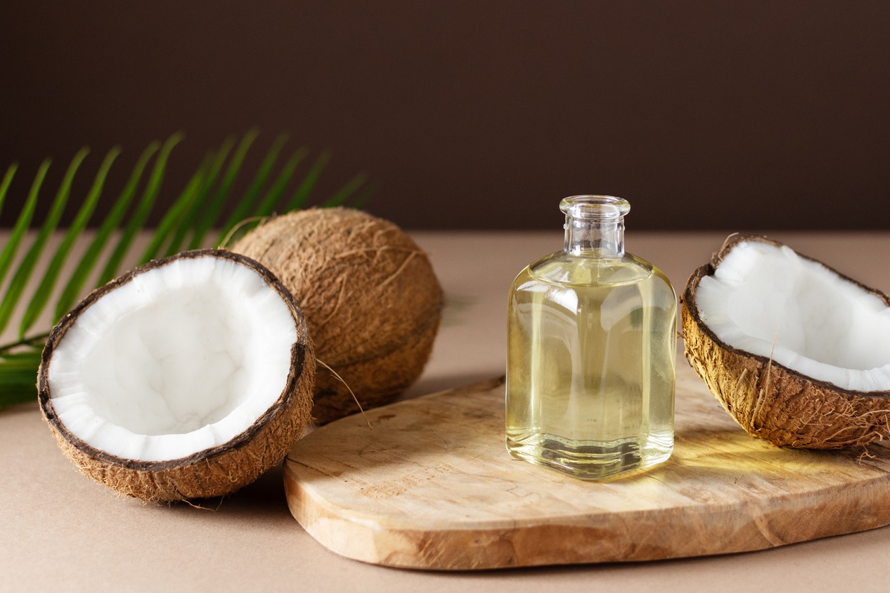 Bottle of coconut oil and fresh coconuts with palm leaf on wooden board over brown background