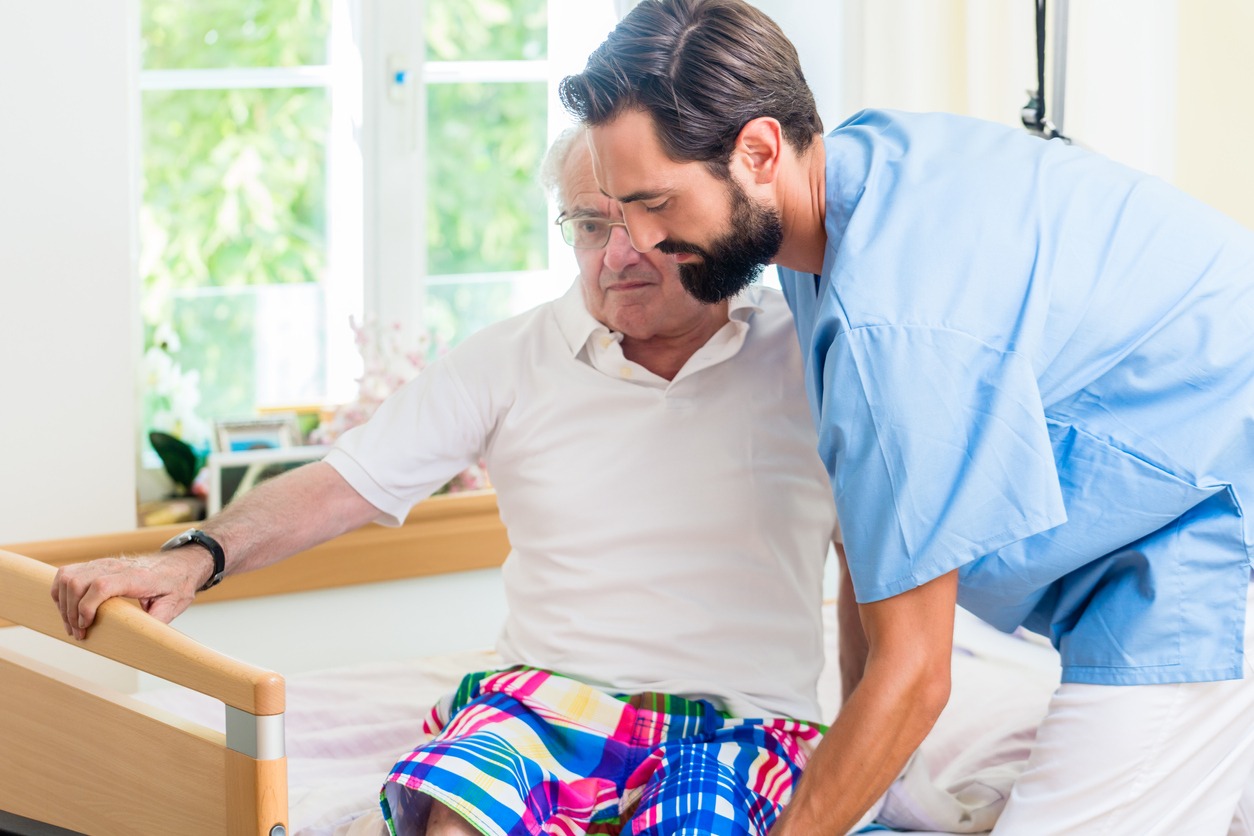 caregiver helping man to get up from the bed