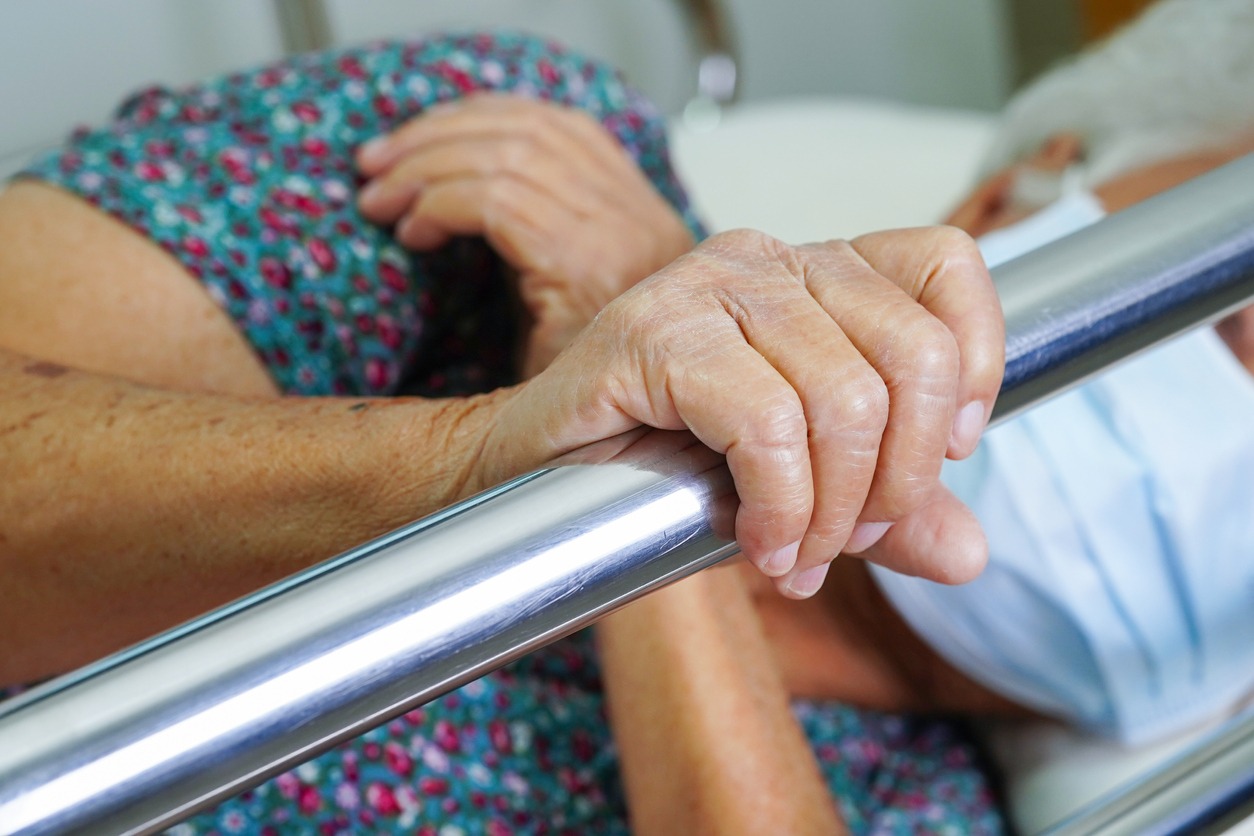 elderly patient holding onto a metal bed rail