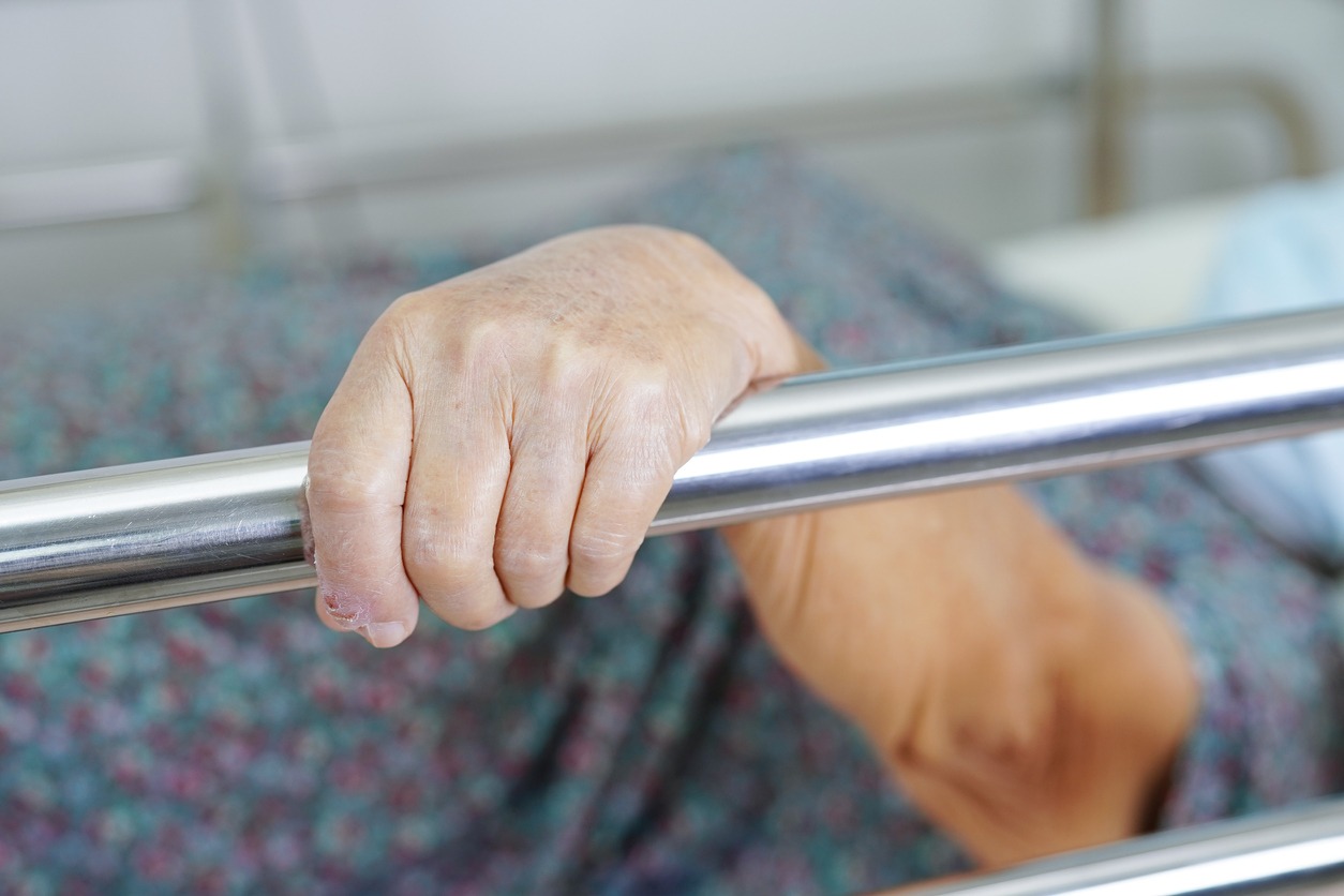 elderly person holding onto a bed rail