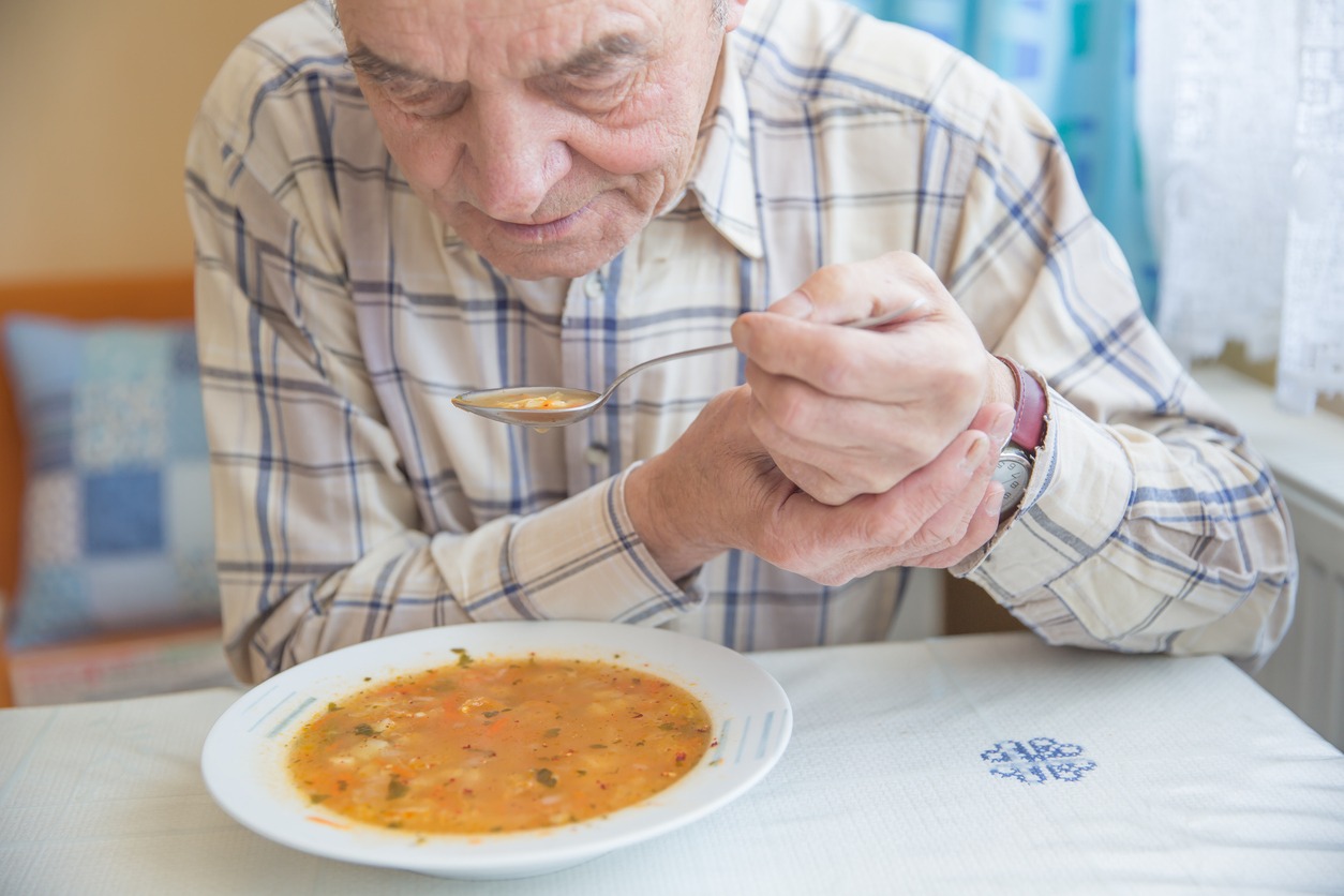 an elderly man with Parkinson’s disease eating soup