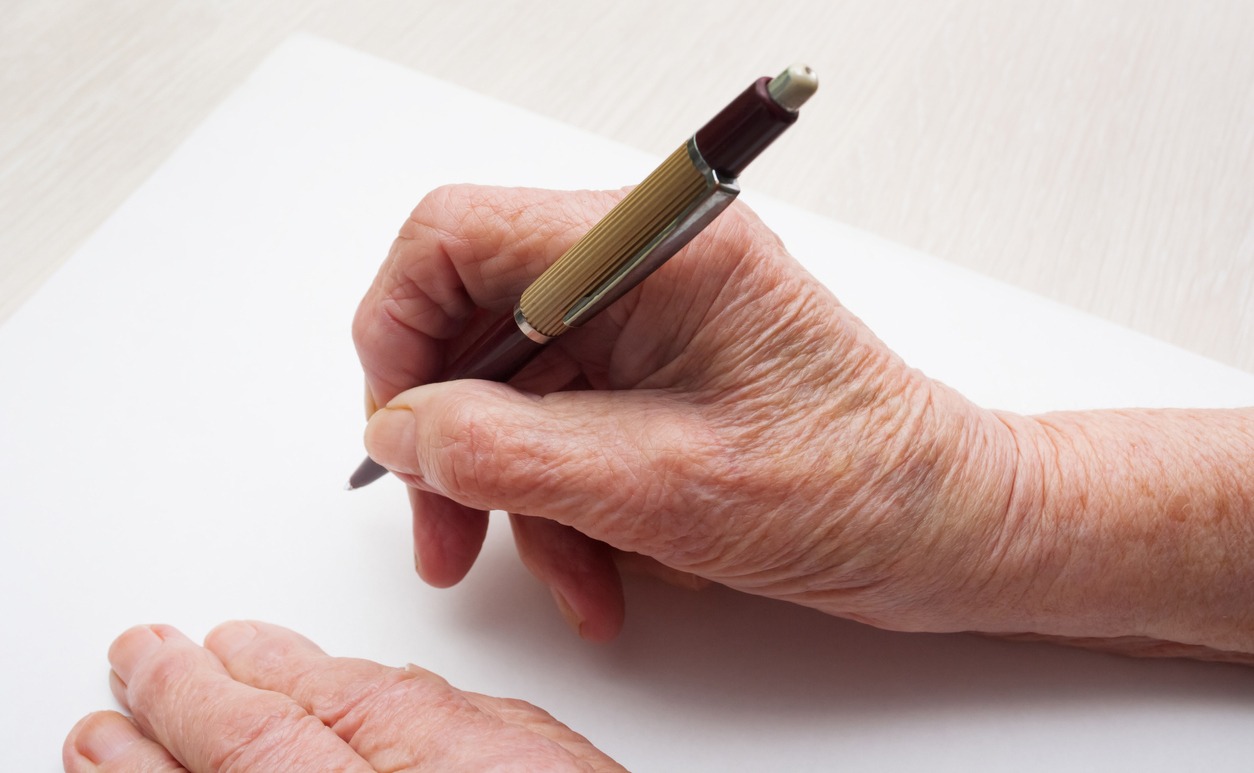 hand of a senior person holding a pen on a sheet of paper