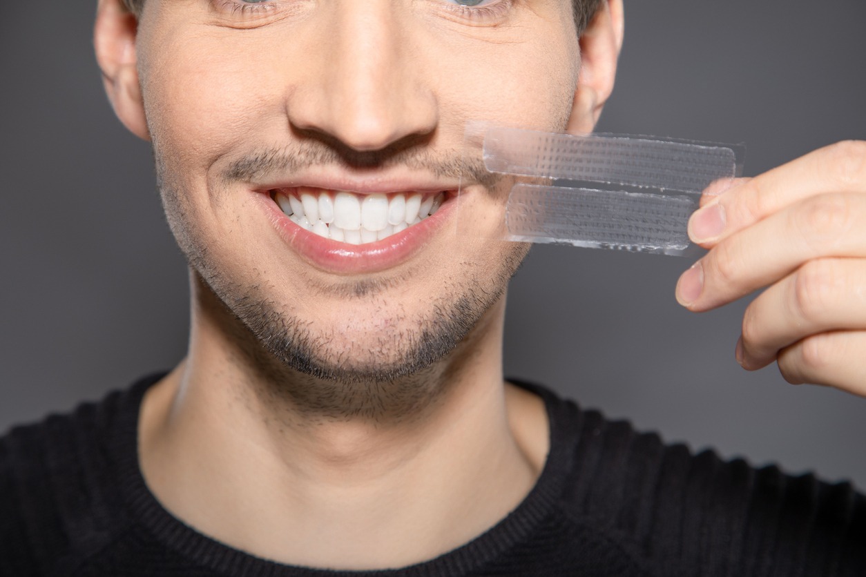 man holding some teeth whitening strips while smiling