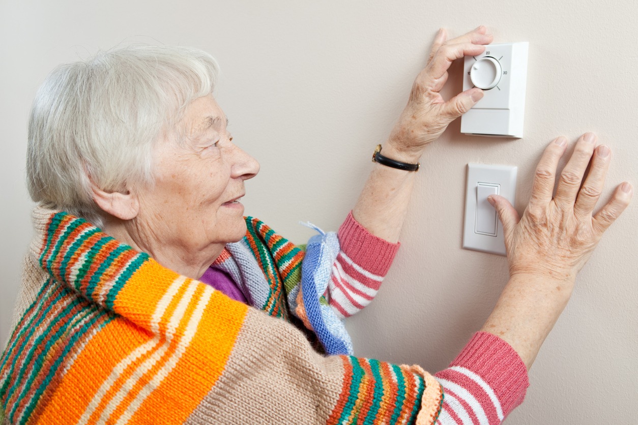 senior woman adjusting the thermostat in her home
