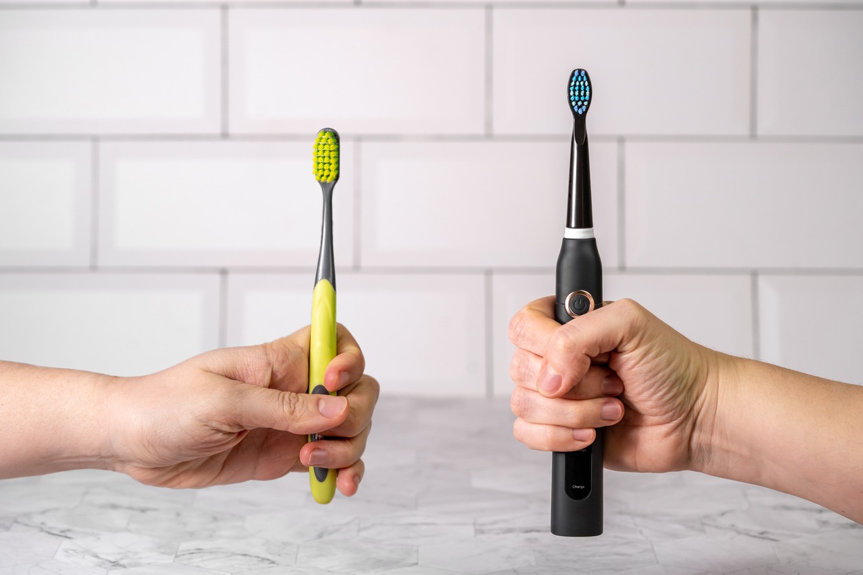 hands holding one electric toothbrush and one manual toothbrush