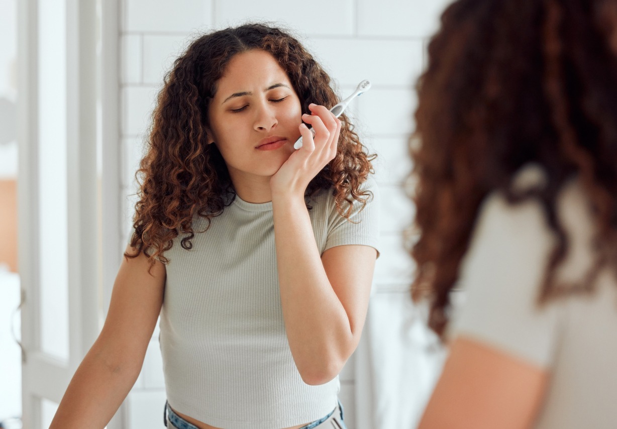 woman feeling discomfort while brushing teeth